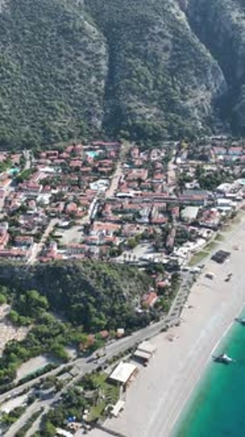 Aerial view of a coastal town nestled against a lush green mountain and turquoise sea