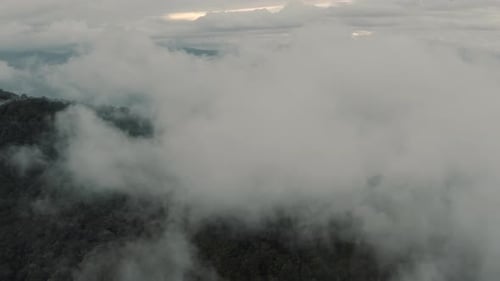 Drone aerial flying high through the clouds over mountain and forest