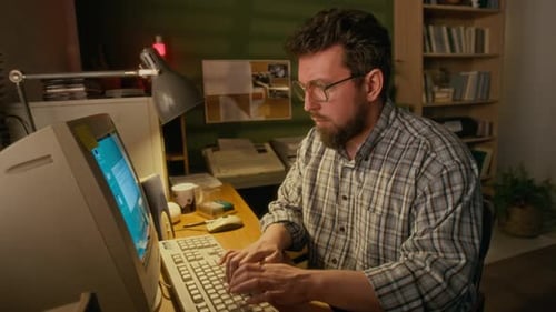 Man Types at Old Computer in Dimly Lit Room
