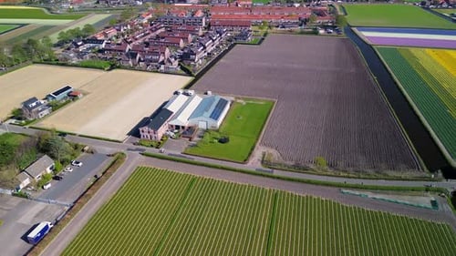 A drone flies over a rural area with neatly cultivated fields, residential houses, green lawns