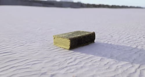 Ancient Book Resting on the Sandy Surface Under Bright Daylight