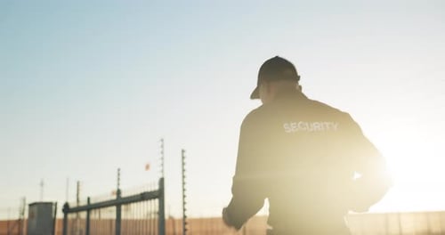 Security Guard Walks Near Gate in Daylight