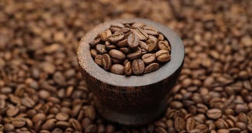 Wooden Bowl Full of Coffee Beans on a Rotating Background of Fresh Roasted Coffee Beans