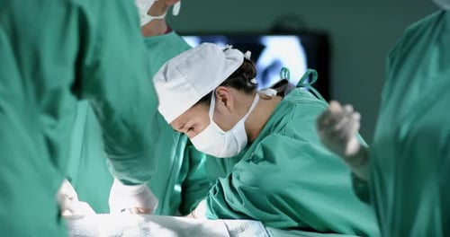 Diverse male and female surgeons operating on patient in operating theatre at hospital, slow motion