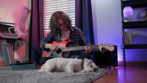 Young Adult Plays Guitar with Dog Nearby