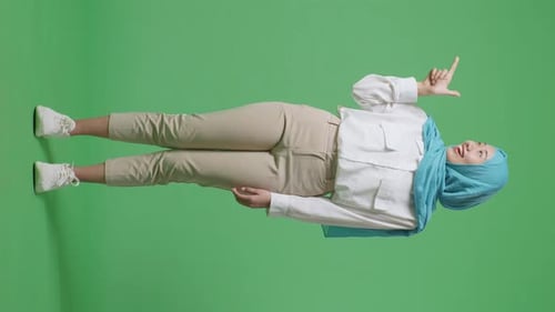 Full Body Of Asian Muslim Woman Smiling And Pointing To Side While Standing In The Green Screen