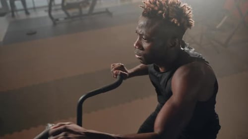 Athletic Black Man with Muscular Arms is Training on Stationary Bike Active Workout in Gym