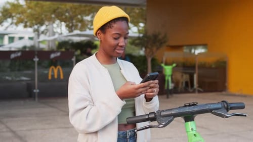 Woman Using Smartphone to Unlock Electric Scooter at Outdoor Rental Station