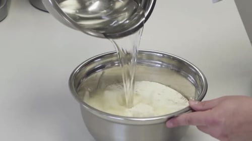 Close-up of adding water to flour while making fresh bread dough.