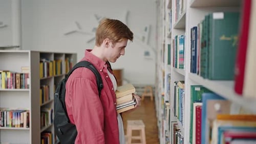 Estudante ruiva procura livros didáticos nas prateleiras da biblioteca