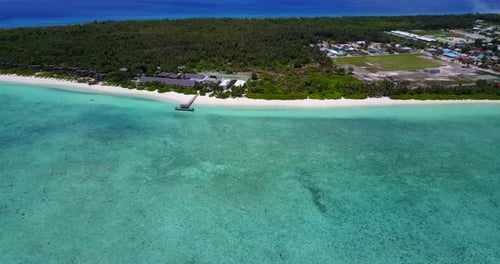 Beautiful coastline of Maldives in Indian Ocean. Soft tilt from clear water towards beach and villag
