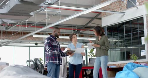 Three diverse happy colleagues discussing while standing together at office