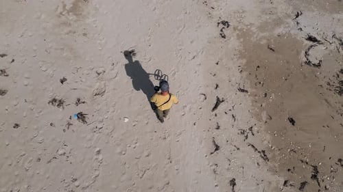 Aerial View of Man Using Metal Detector on Sandy Beach Searching for Treasure Among Footprints and