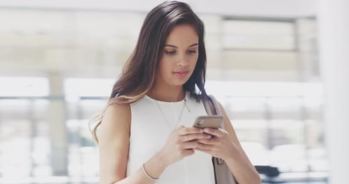 4k video footage of a young businesswoman using a cellphone while walking in a modern office