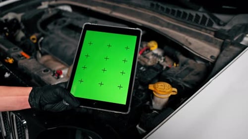 Close-up of a hand with a tablet on which the green screen is open against the background of a car