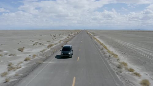 Coche conduciendo rápido en una carretera abierta en el desierto, vuelo aéreo hacia atrás