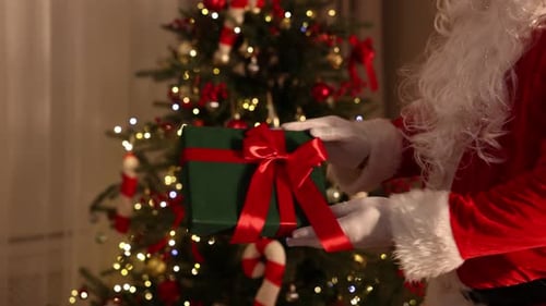 Weihnachtsmann schenkt Frau in der Nähe des Weihnachtsbaums drinnen eine Geschenkbox, Nahaufnahme