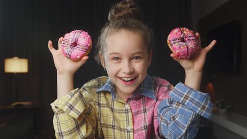 Portrait of a Caucasian Child in a Pink Shirt Holds Two Pink Glazed Donuts in His Hands Near His
