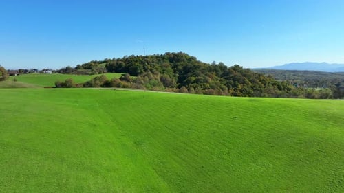 Vast green field on a sunny day with rolling hills, woods, and clear blue sky in the background