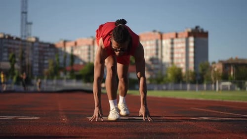 Zeitlupe Ein männlicher Athlet mit Sonnenbrille und Dreadlocks auf dem Kopf nimmt die Startposition in der Hocke ein