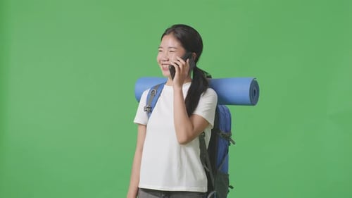 Asian Female Hiker Smiling And Talking On Smartphone While Standing On Green Screen