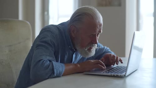 Side View of Senior Adult Male Sitting with Laptop and Looking at Screen with Concerned Facial