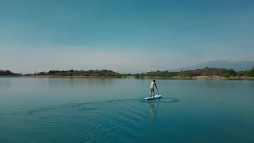 Aerial drone flying over a man doing stand up paddle in a blue water lake with mountains