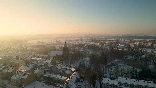 Aerial orbit shot of beautiful snowy cityscape with church and snowy houses in Poland during sunset