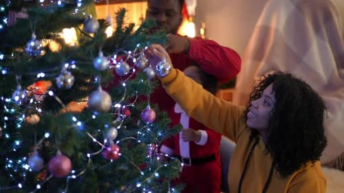 Side View Smiling African American Young Woman Decorating Christmas Tree with Man and Little Boy on