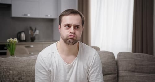 Upset Man Sitting on Couch Covering Ears