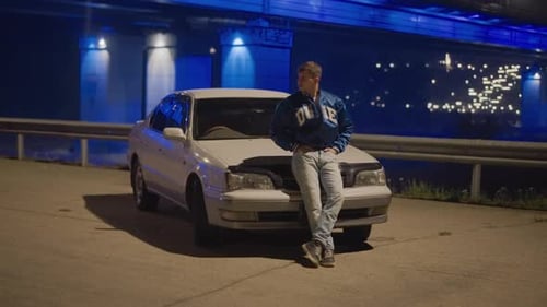 Young Man Leans on Car at Night