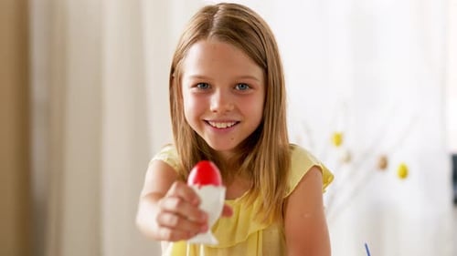 Glückliches Mädchen zeigt an einem Frühlingsurlaub zu Hause in Zeitlupe ein farbiges Osterei