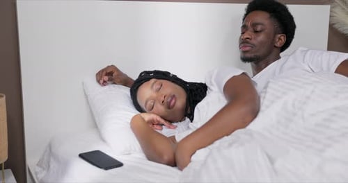 Família feliz: esposa e marido de pele escura dormindo deitados na cama. Homem curioso verificando a hora