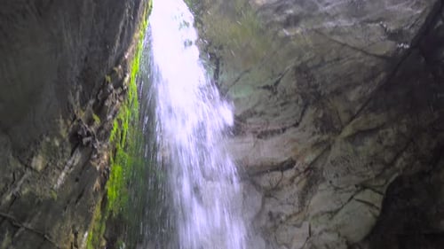 A small cave with big waterfall splashing down forming small pool of water. tight space with moss on