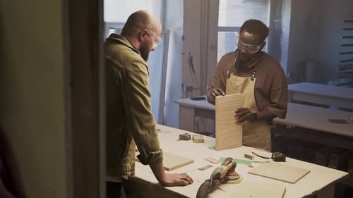 Two Multi-Ethnic Woodworkers Discussing Material in Furniture Workshop