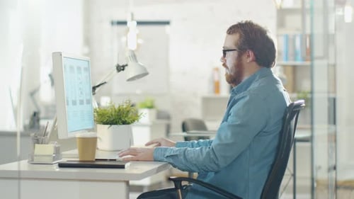 Young Bearded Man Working on Personal Computer while Sitting in His Creative Agency Office.