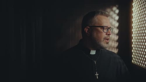 Catholic Priest Speaking to Penitent from inside of Confessional Booth