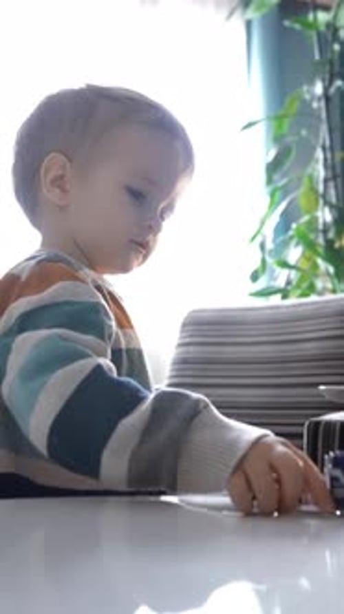 Vertical of Joyful Boy Explores Toys on Table Amidst Fleeting Light at Home