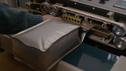 Hands of Specialist Using Machine to Pack Roasted Coffee Grains