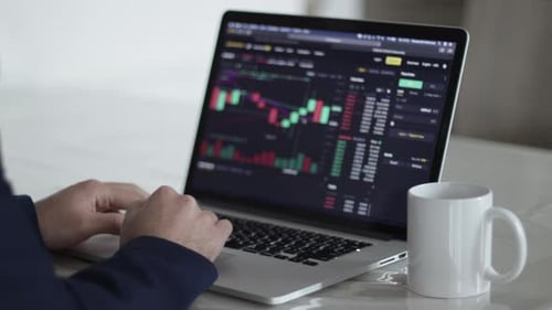 Man Typing on Laptop with Stock Market Data