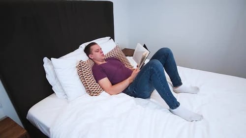 Man Reading Book Lying on Bed Indoors