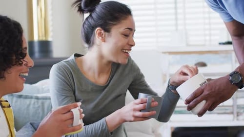Three happy, diverse female and male friends having coffee at home, in slow motion