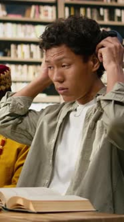 Vertical Video Student Adjusting Headphones at Library Study Desk with Computer