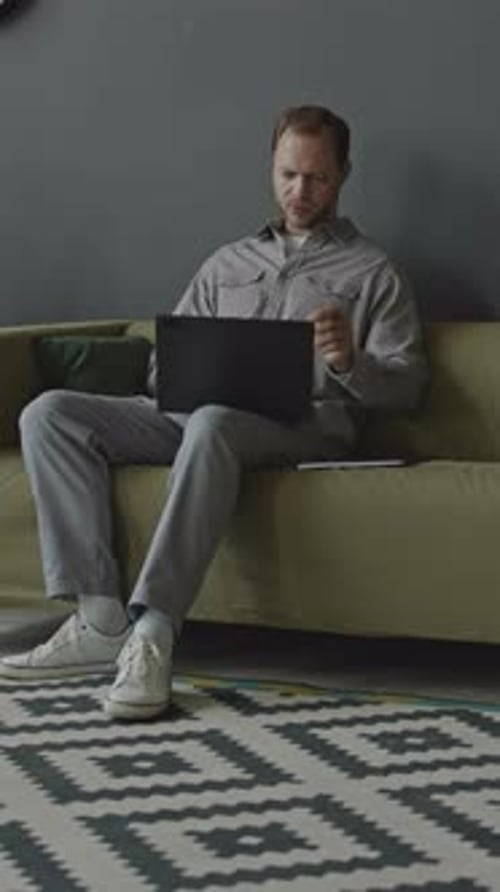 Young Man Video Conferencing on Laptop on Couch in Office