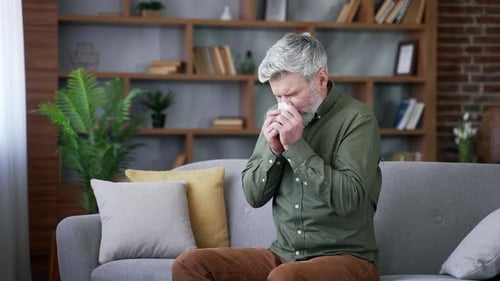 Man With Gray Hair Blows Nose On Couch