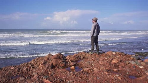 Mann mit Hut am Felsenstrand blickt auf den Atlantik in Marokko Sommerurlaub