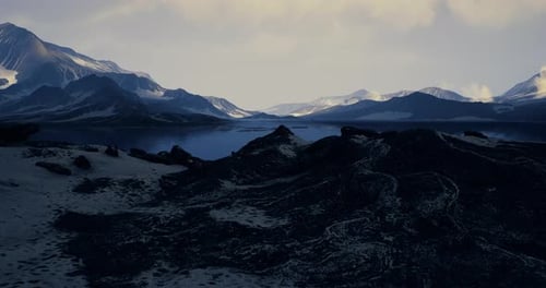 Mountain Landscape with Dark Rocks and Distant Snowy Peaks Under Cloudy Sky