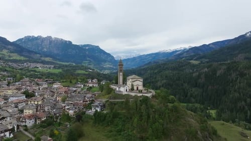 Slow aerial push towards a church on a hill outside of a town in northern Italy.