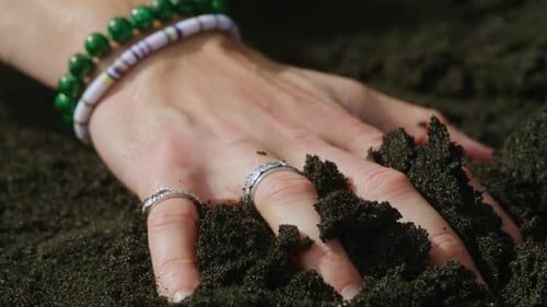 A Hand Grasps Dark Soil Adorned with Beautiful Jewelry Accents Creating a Striking Contrast