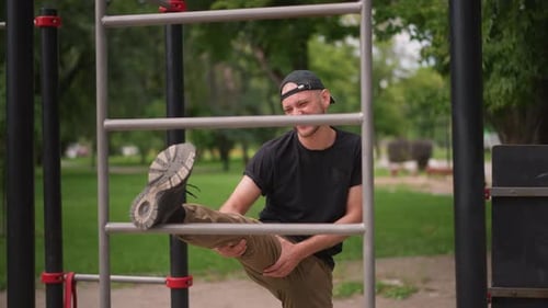 Casual Man Warming Up With Leg Stretches On Metal Bars Smiling Man In Casual Attire Engaging In Leg